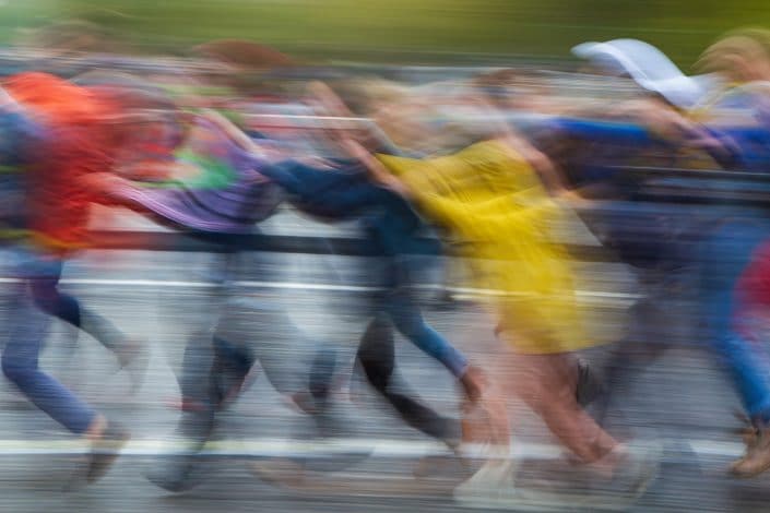 several people run together in a line, blurred so that they appear as a colourful wave more than individuals.