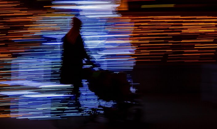 A mother pushes a stroller in the dark, sillhouetted by thousands of bright lights