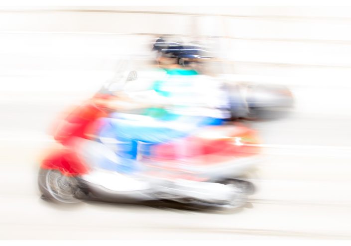 A blurred image of a person on a scooter with bright colours.